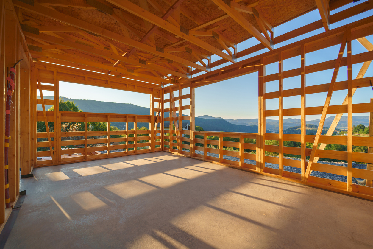 Interior of a wooden framed house under construction with mountain views through open window spaces.