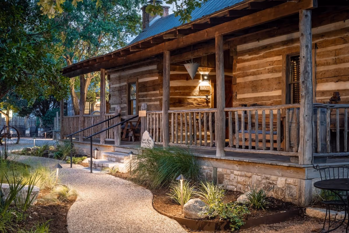 Rustic log cabin with wooden porch, landscaped pathway, and evening lighting