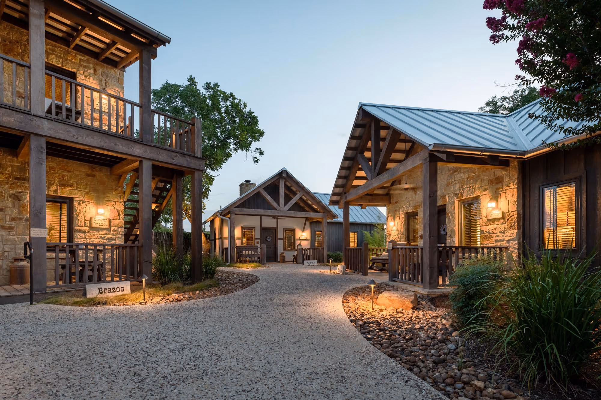 Rustic stone cabins with warm lighting at dusk, surrounded by landscaped path