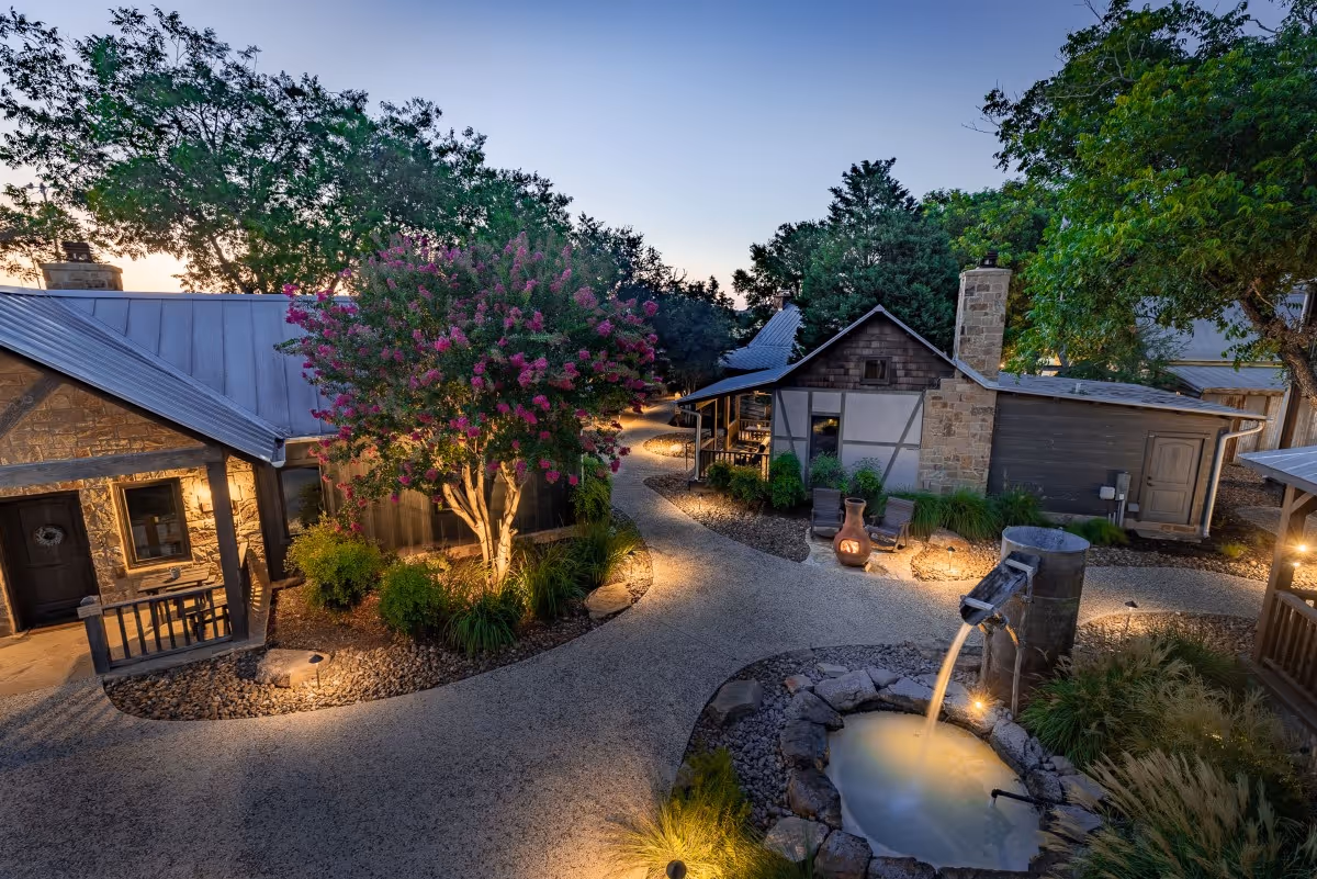 Twilight landscape with stone cottages, flowering tree, and tranquil water feature