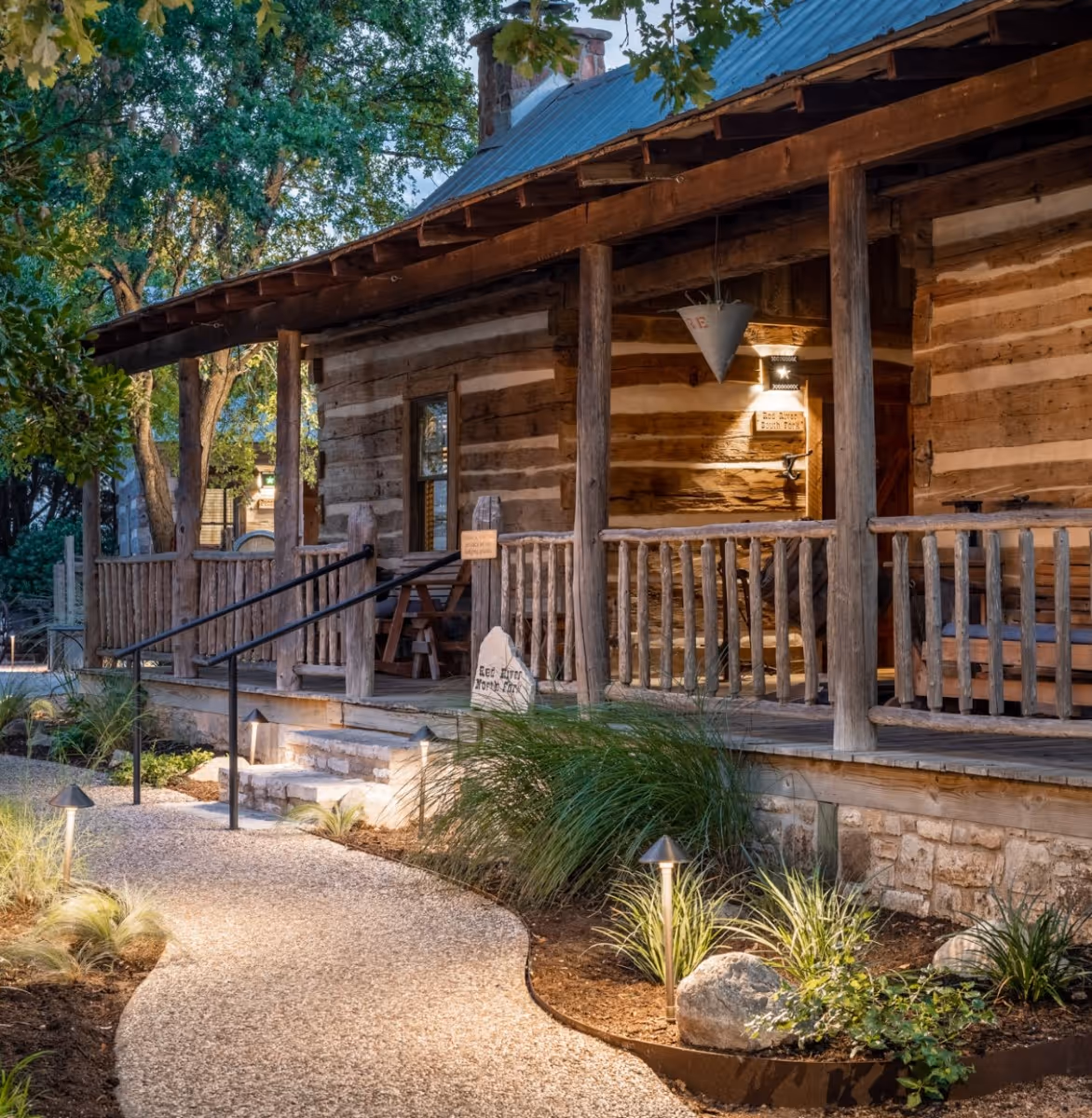 Historic log cabin guest accommodation with covered porch and landscaped walkway at a charming Bed & Breakfast in Fredericksburg, Texas