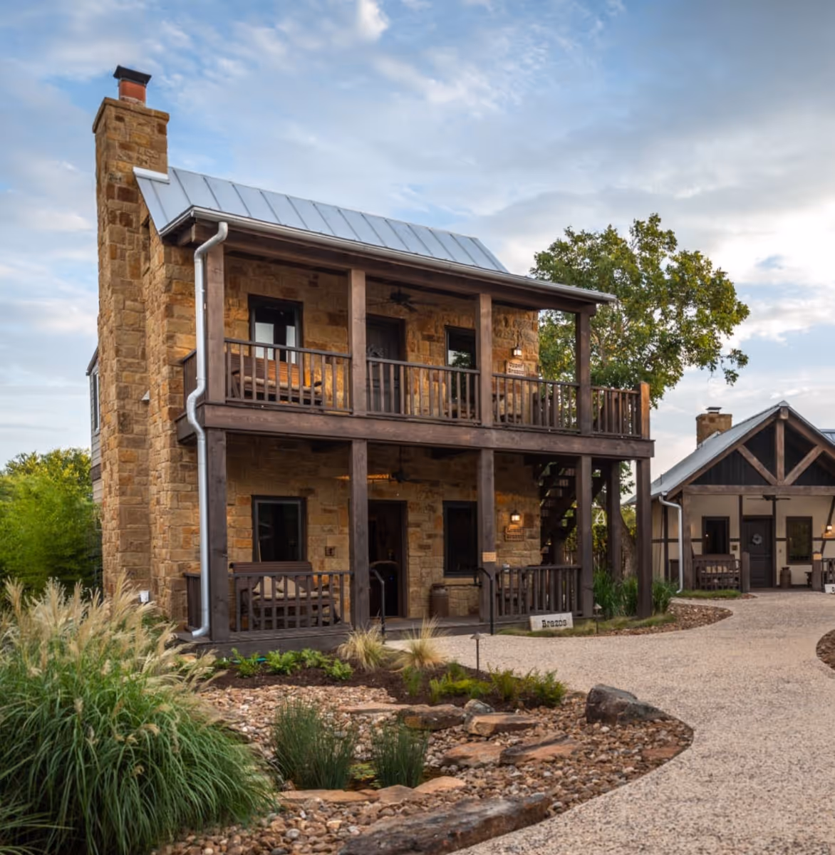 Two-story stone cottage with covered balconies and metal roof at a luxury Fredericksburg Bed & Breakfast surrounded by native landscaping