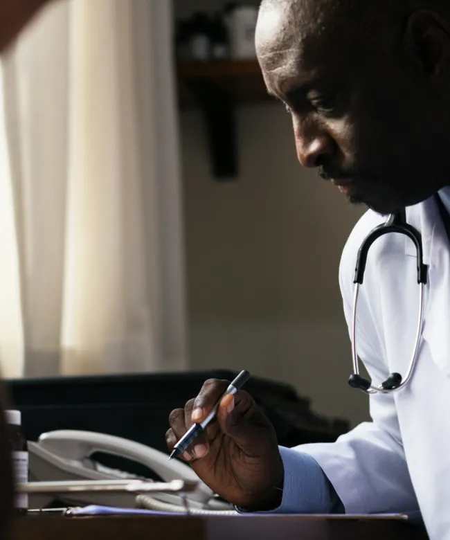 SmartCare Rx Pharmacy doctor consulting attentively with a patient at a desk, writing medical notes during a clinical visit.