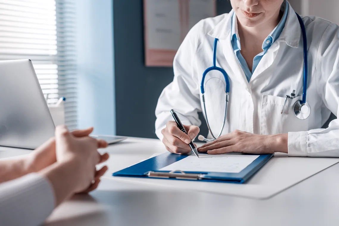 SmartCare Rx Pharmacy healthcare provider consulting with a patient at a desk, attentively writing medical notes during a clinical visit