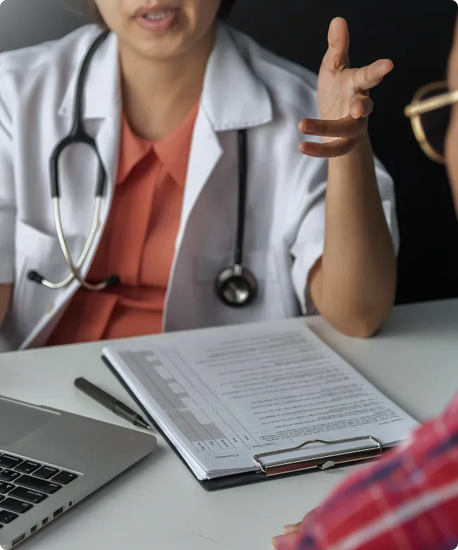 SmartCare Rx Pharmacy female doctor in a white coat consulting with a patient, discussing medical information with a clipboard and laptop during an appointment, highlighting attentive clinical care