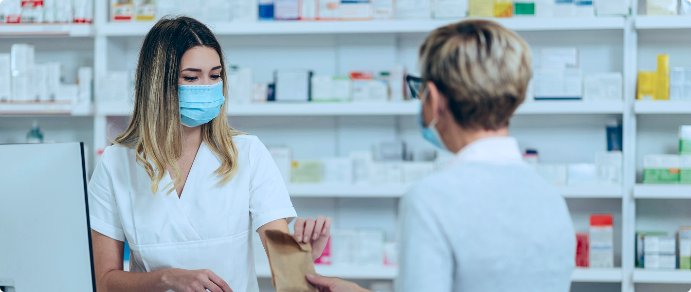 SmartCare Rx Pharmacy pharmacist handing a paper bag containing medication across the counter to a customer in a well-organized pharmacy, highlighting personalized prescription service