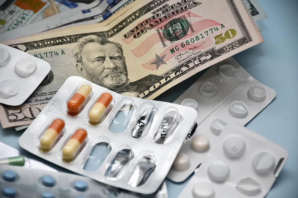 SmartCare Rx Pharmacy various blister packs of pills and capsules placed on top of U.S. dollar bills, illustrating the connection between medication costs and pharmacy expenses