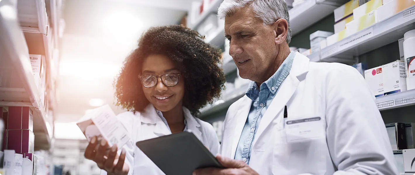 SmartCare Rx Pharmacy pharmacists collaborating in a modern pharmacy, reviewing medication boxes and a digital tablet to ensure accurate prescription management