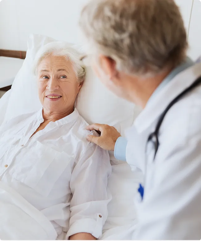 SmartCare Rx Pharmacy male doctor providing bedside support to a smiling elderly female patient in a hospital setting, showcasing compassionate inpatient care.