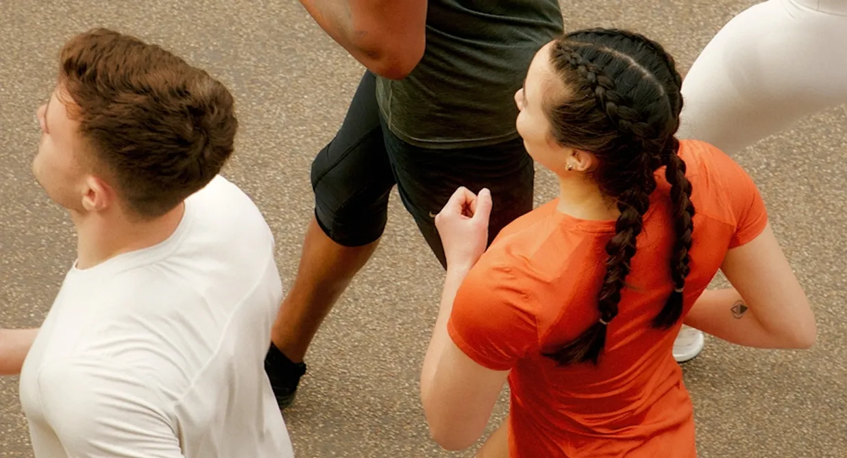 Four people, seen from above, jog together on a paved path -embracing weight loss and longevity. One wears orange, another white, and their hair and skin tones vary.