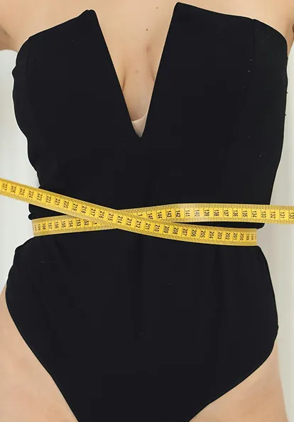 Person's torso wrapped with yellow measuring tape showing waist measurement