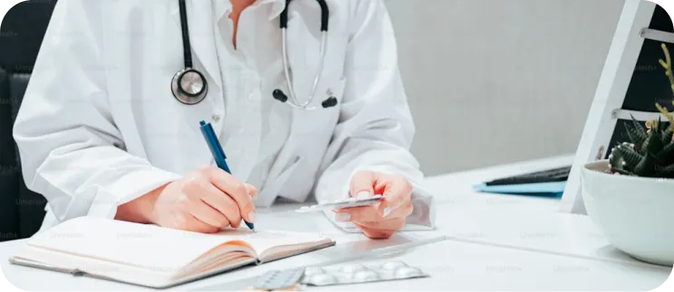 Doctor in white coat with stethoscope writing notes at desk with medications