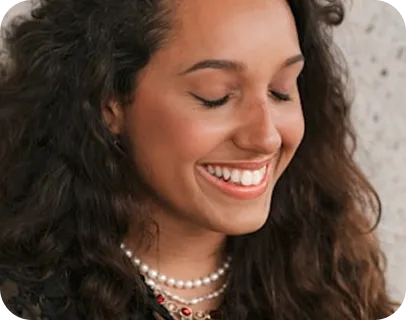 Woman with long dark wavy hair smiling wearing pearl necklace