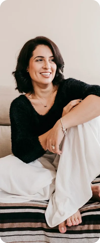 Smiling woman with dark wavy hair sitting on bed in black and white outfit