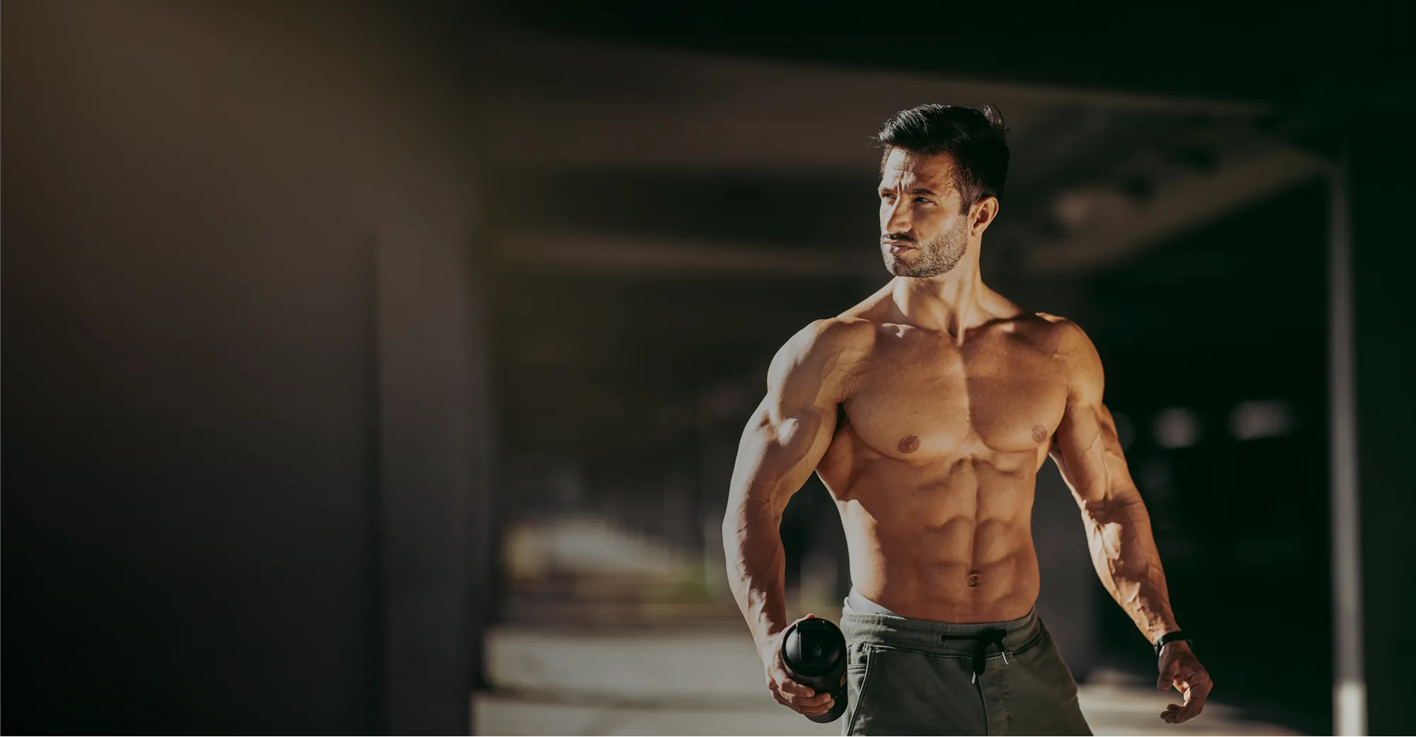 Shirtless muscular man holding dumbbell in industrial setting