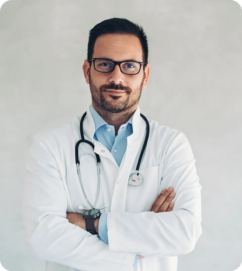 Professional male doctor wearing white coat, glasses, and stethoscope, arms crossed, smiling.
