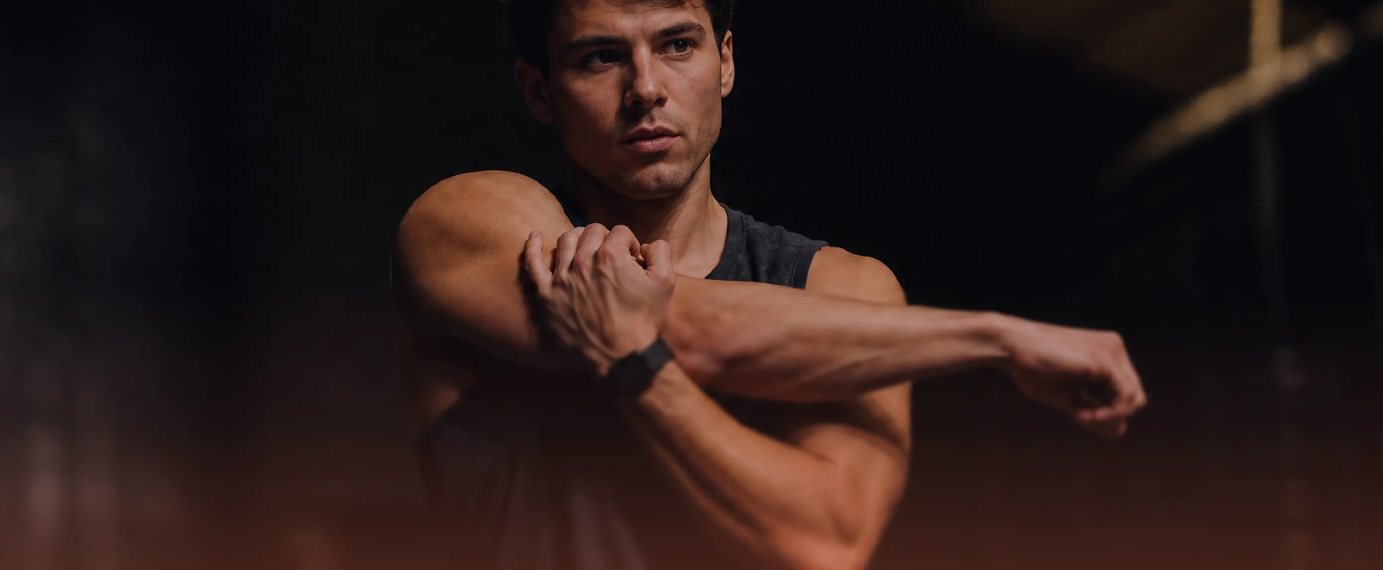 Muscular man in dark athletic shirt flexing arms against black background