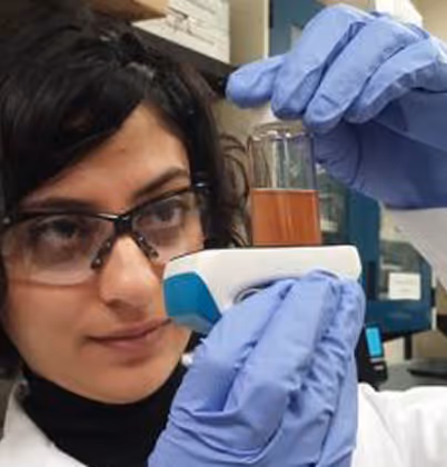 Scientist wearing glasses and blue gloves holding a test tube with orange liquid in a lab.