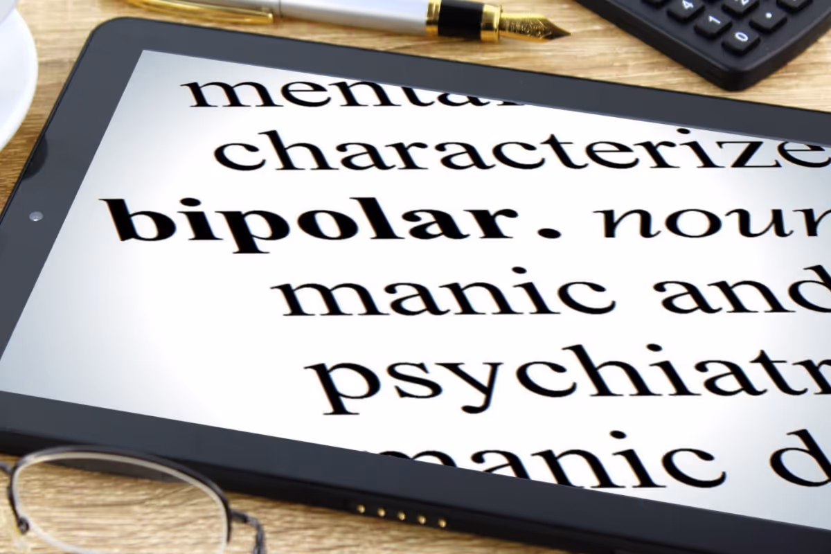 Tablet screen displaying the word 'bipolar' in a dictionary-like text with glasses, pen, and calculator on a wooden desk.