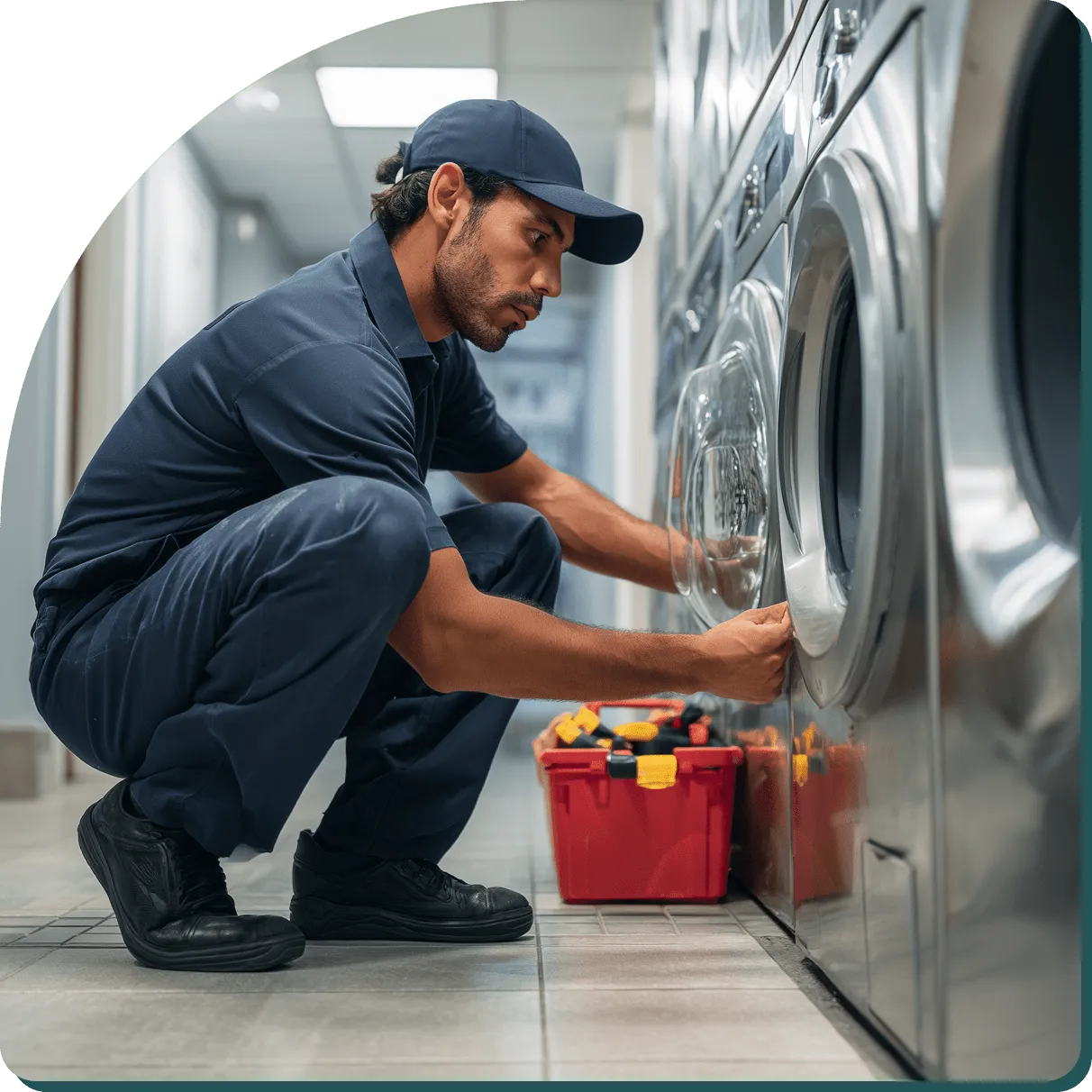 Technician repairing commercial laundry machine in uniform with tool kit.