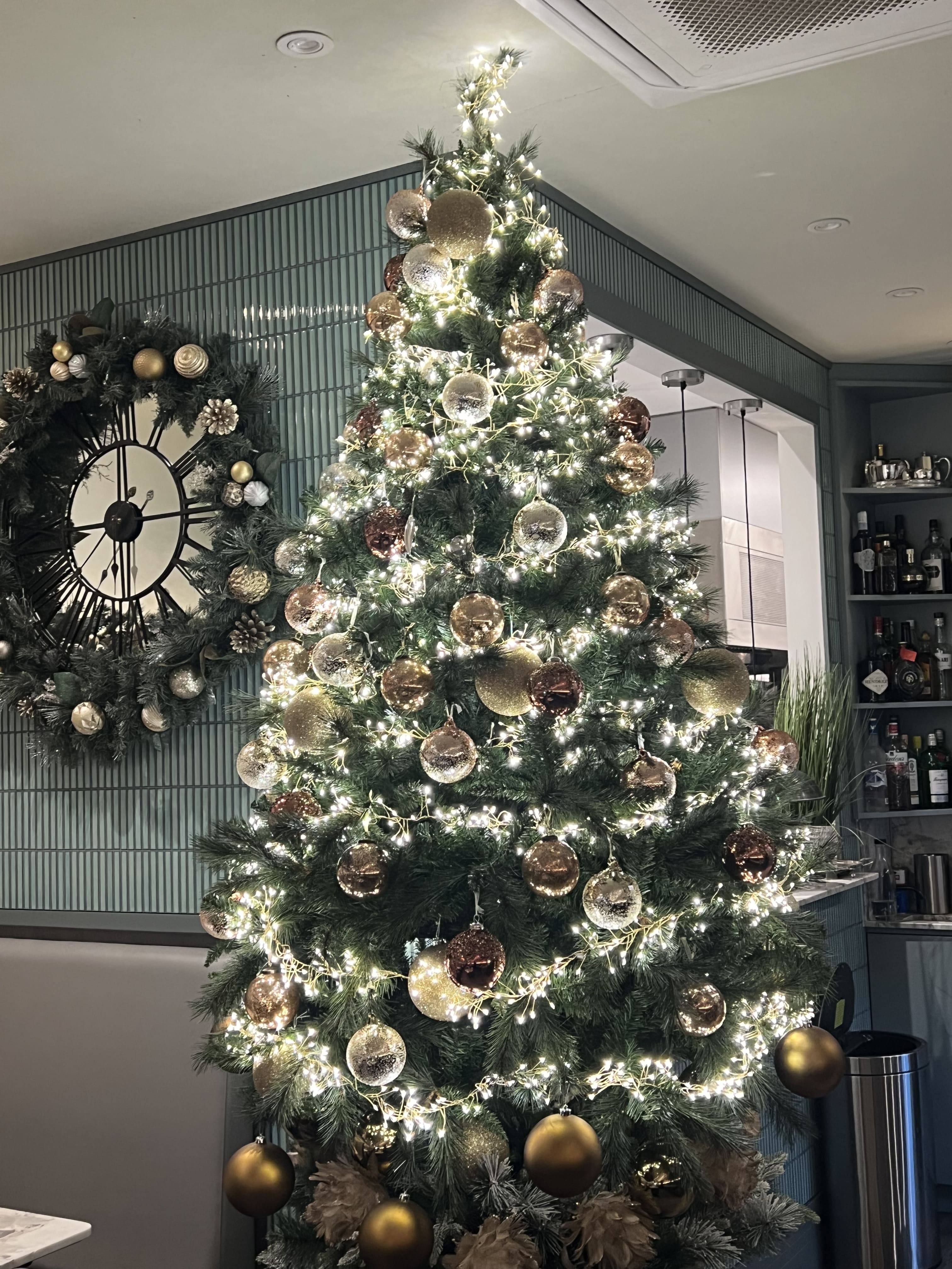 Festive Christmas decorations at Paolo’s Italian Kitchen — a beautifully lit Christmas tree with gold and bronze baubles beside a wreath-adorned clock, creating a warm and elegant holiday atmosphere.