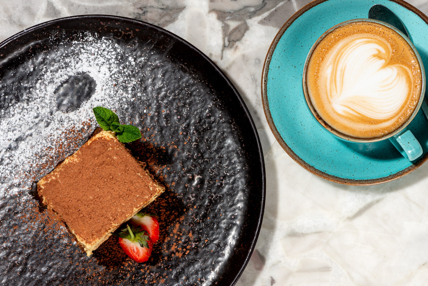 Classic Italian tiramisu dusted with cocoa and fresh strawberries, served with a creamy cappuccino featuring heart-shaped latte art at Paolo’s Italian Kitchen.