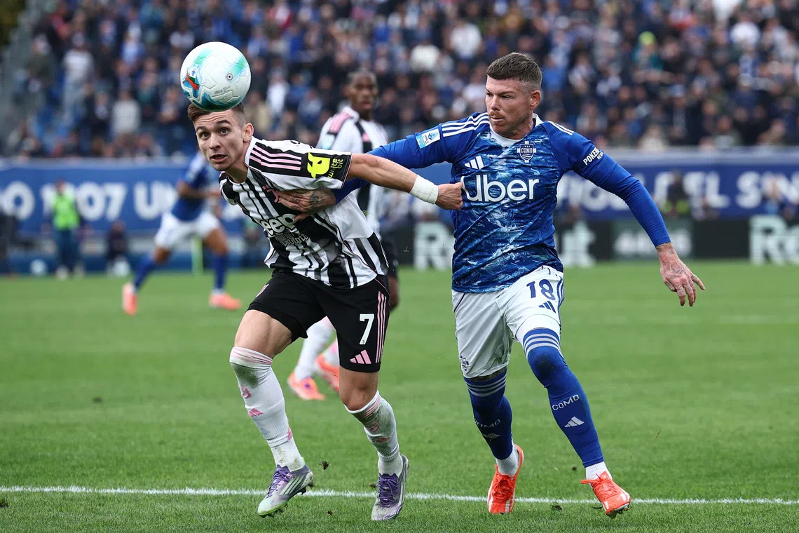 Two soccer players competing for the ball, one heading it while the other tries to hold him back on a grass field.