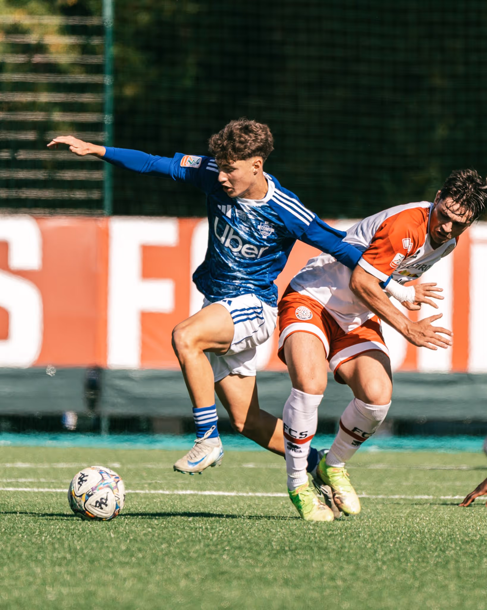 Two soccer players competing for the ball on a green field during a sunny match.