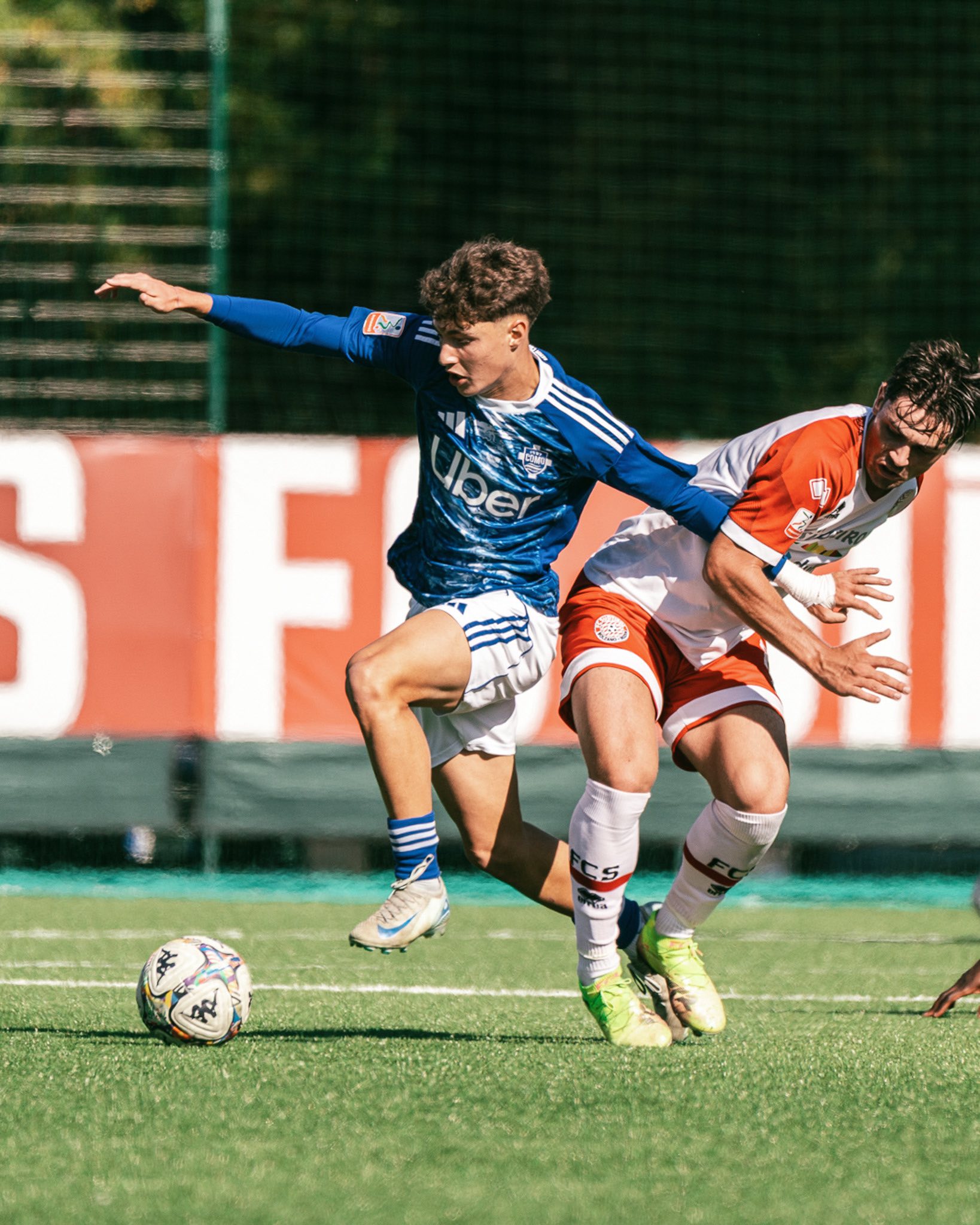 Two soccer players competing for the ball on a green field during a sunny match.