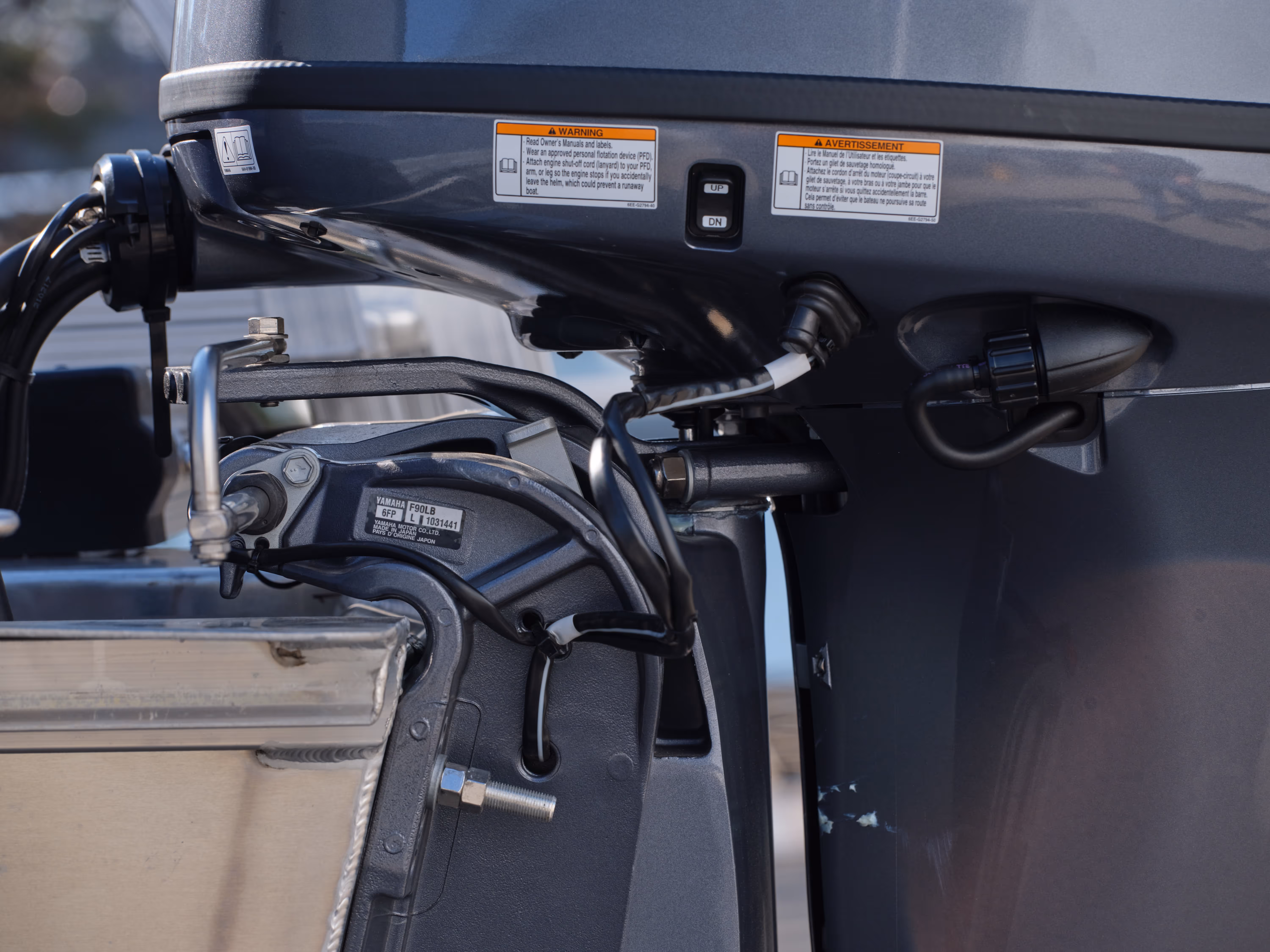 Close-up of a Yamaha F90LB marine outboard motor attached to a boat transom, showing wiring and adjustment controls.