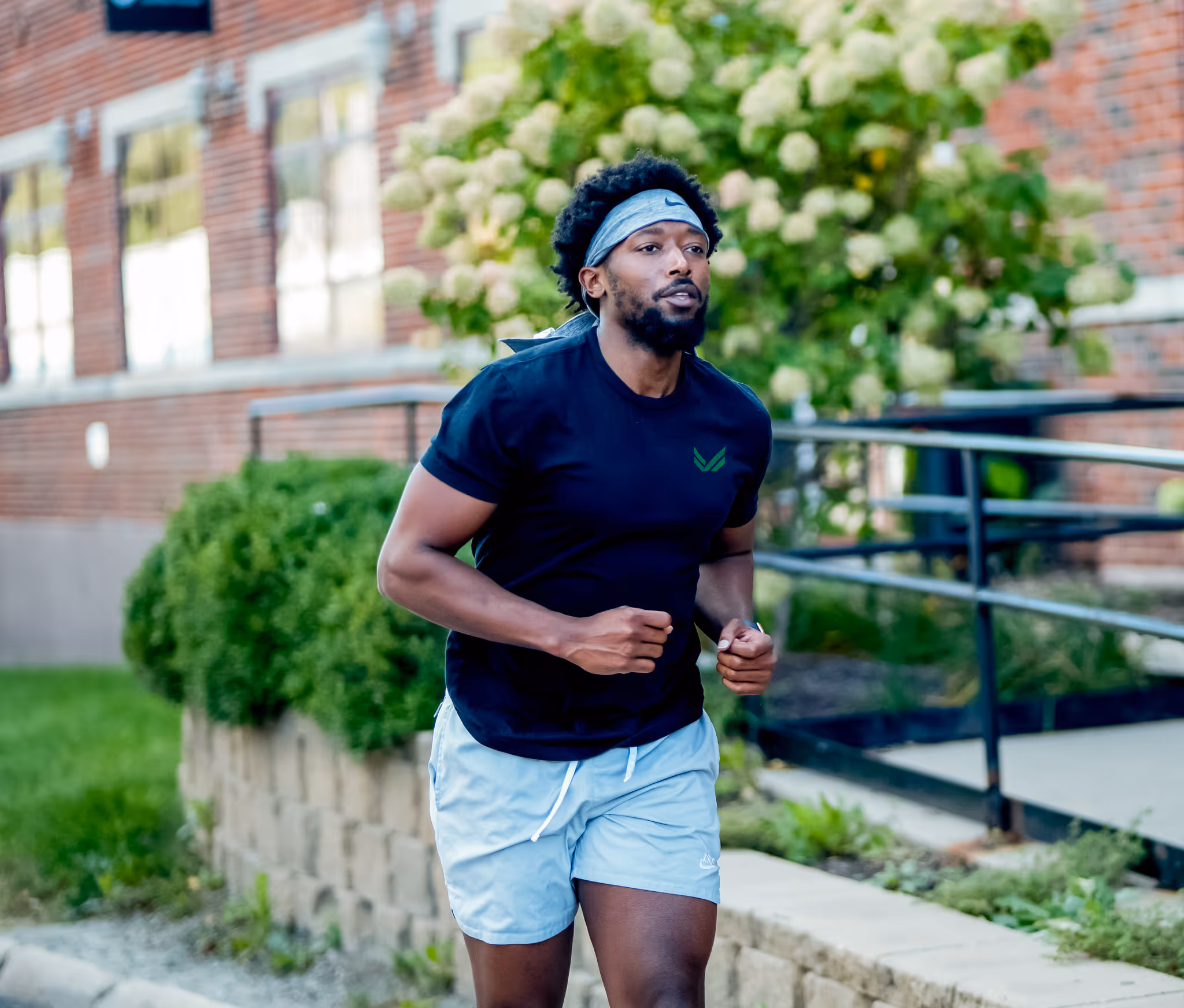 Man jogging outdoors wearing a black t-shirt, light blue shorts, and a gray headband.