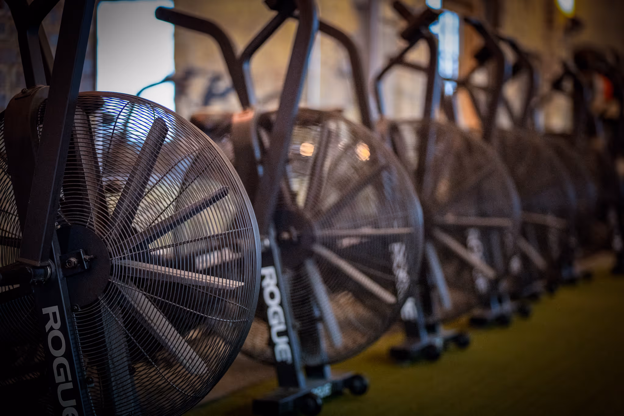 Row of stationary air bikes with large fan wheels in a gym.