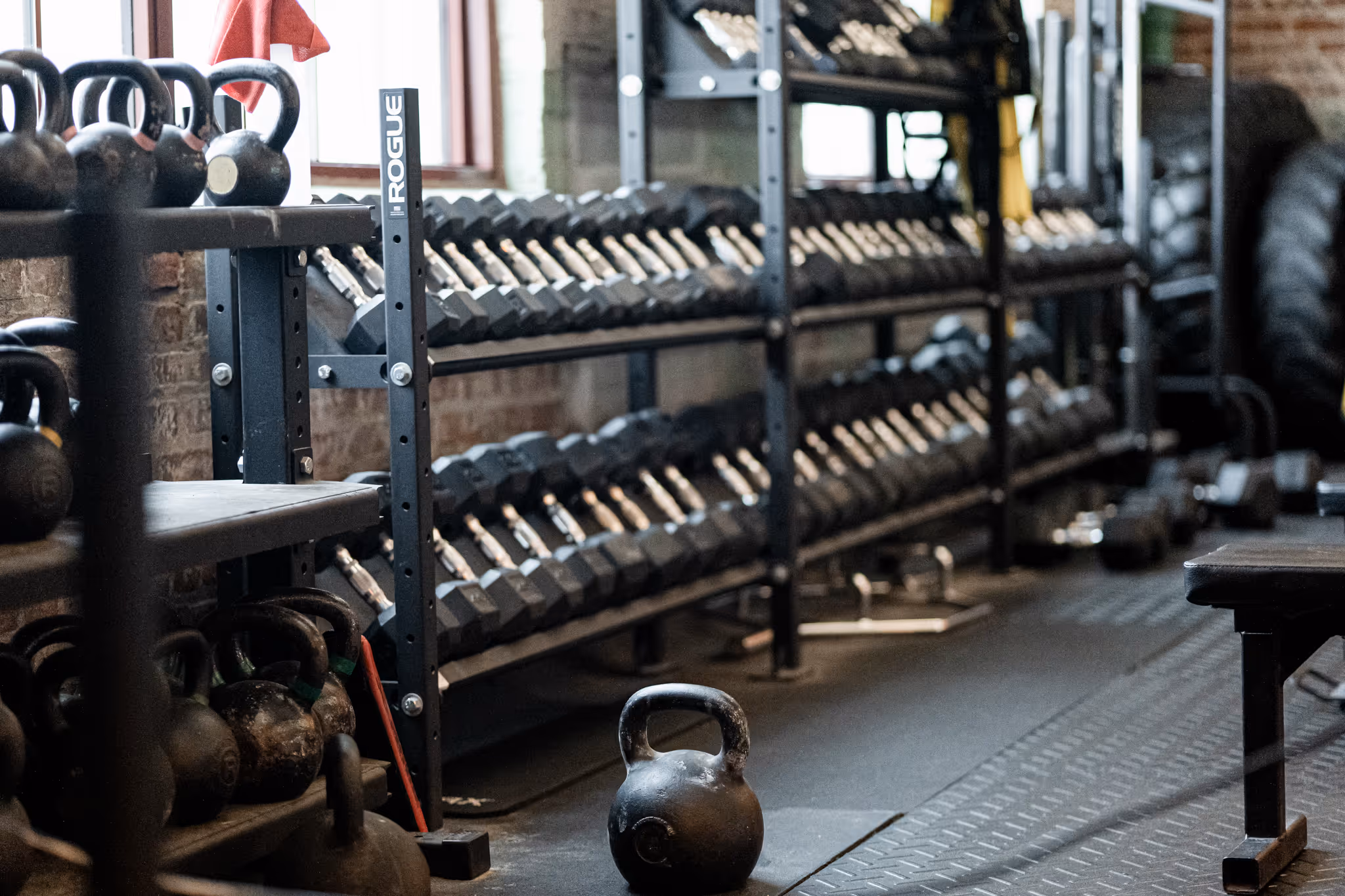 Kettlebell on the floor in front of shelves stocked with kettlebells and dumbbells in a gym.