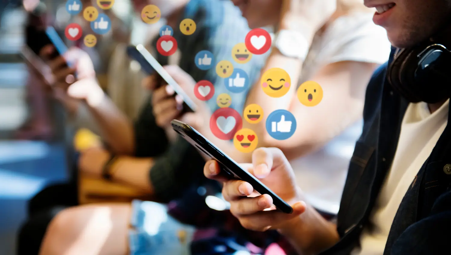a line of teens looking at their cell phones and a bunch of emojis animated from the devices