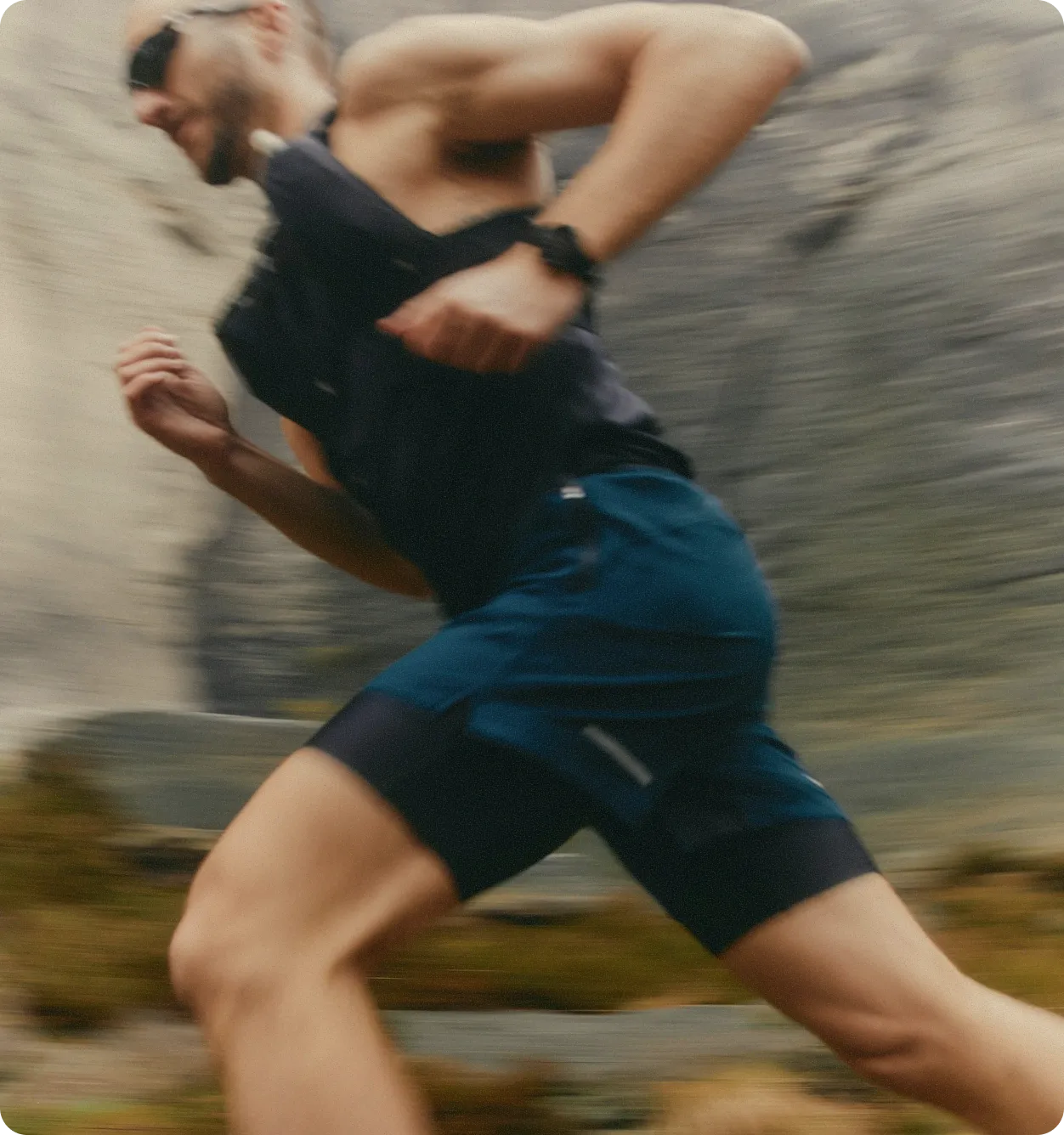 A person wearing a sleeveless shirt, shorts, and sunglasses is running outdoors on a blurred background of rocks and mossy terrain, embracing a science-based care approach for their personalized plans.