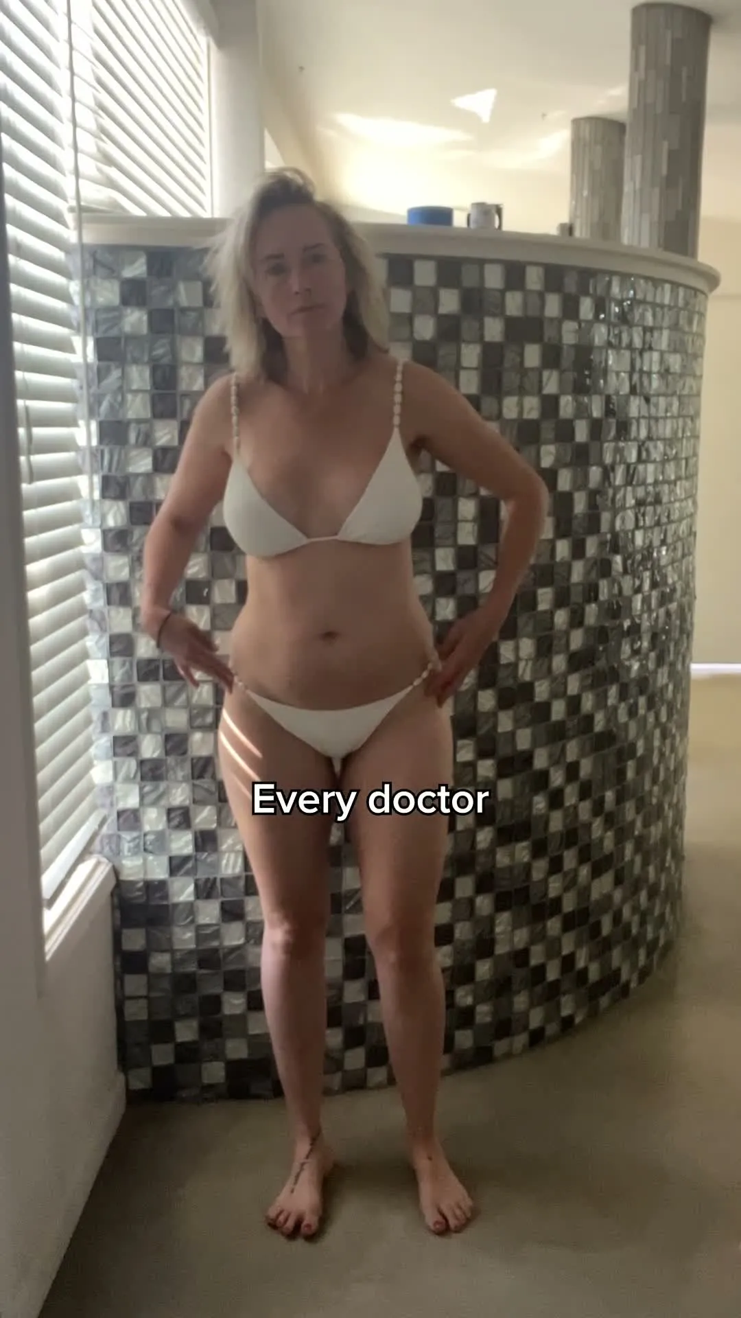 Woman in white bikini posing in bathroom with checkered tile walls