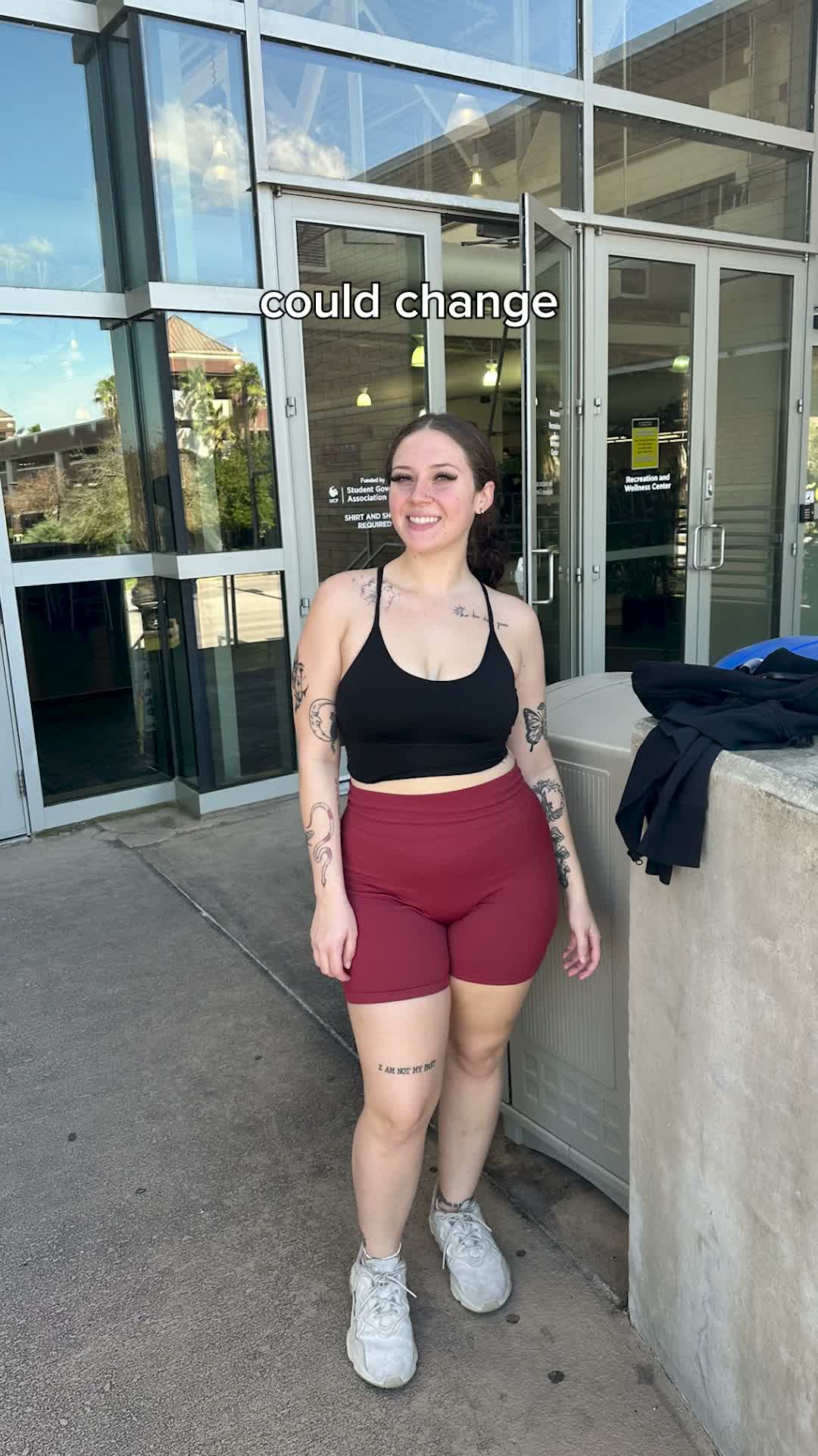 Woman in black crop top and maroon shorts standing outside modern building entrance