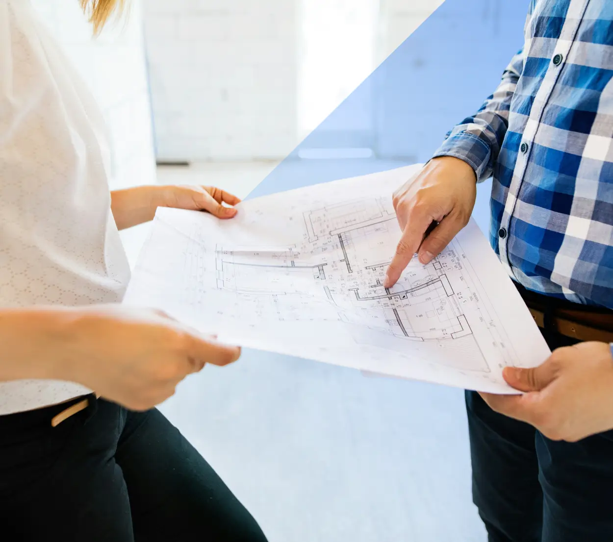 Two people holding and reviewing architectural blueprints, one pointing to a detail on the plan.