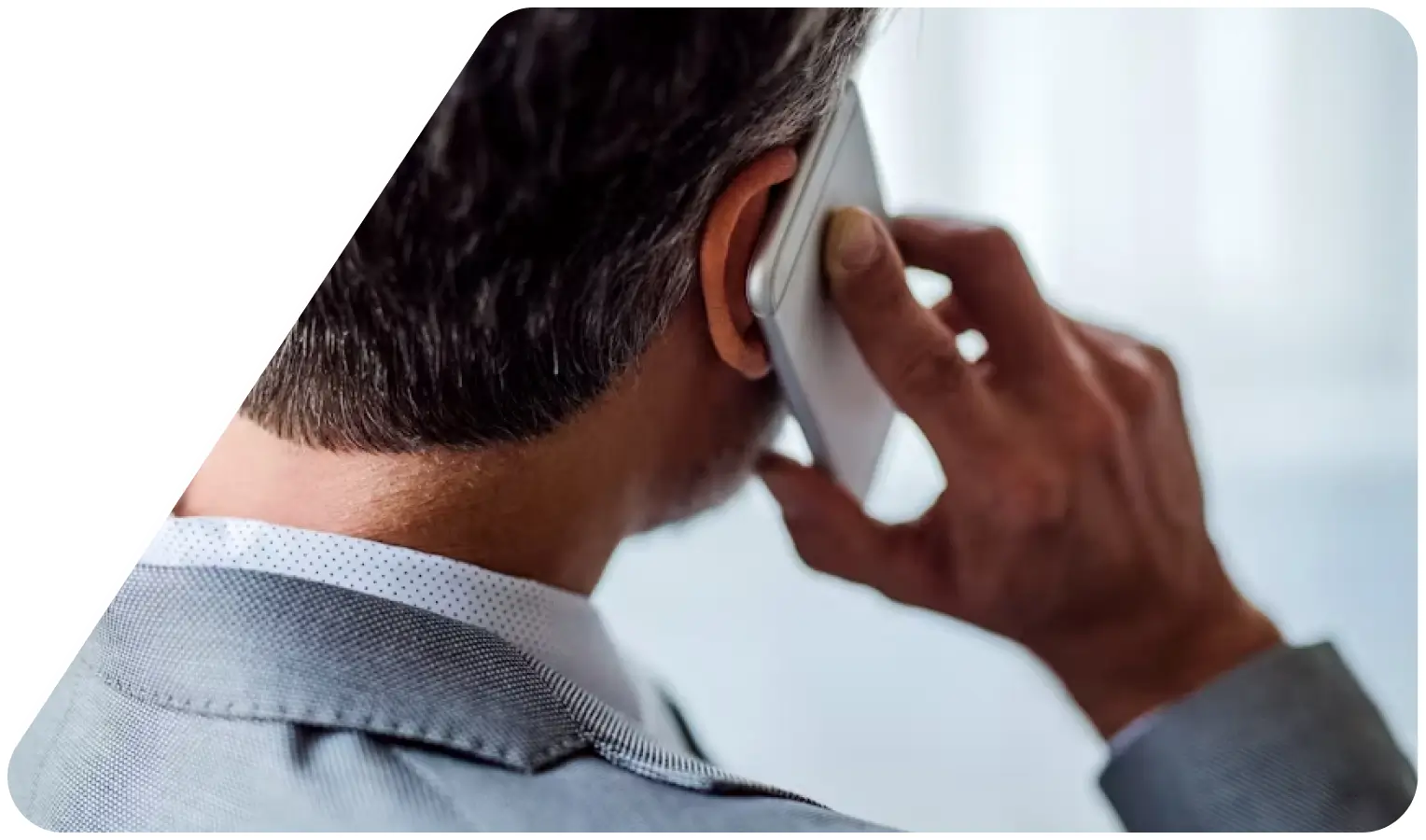 Man in a gray suit talking on a smartphone, viewed from behind.