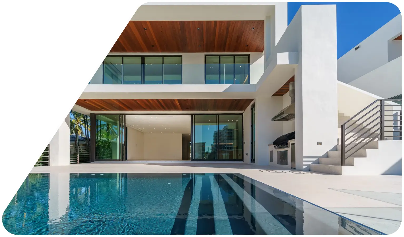 Modern luxury home with a glass balcony, wooden ceiling accents, an outdoor kitchen, staircase, and a blue swimming pool.
