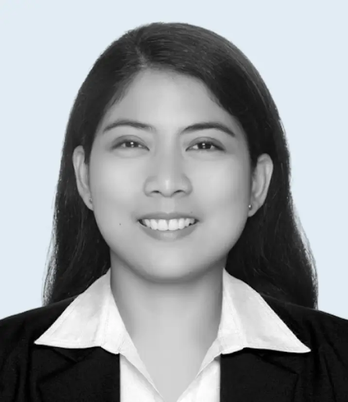 Smiling woman with long dark hair wearing a white collared shirt and black blazer against a light background.