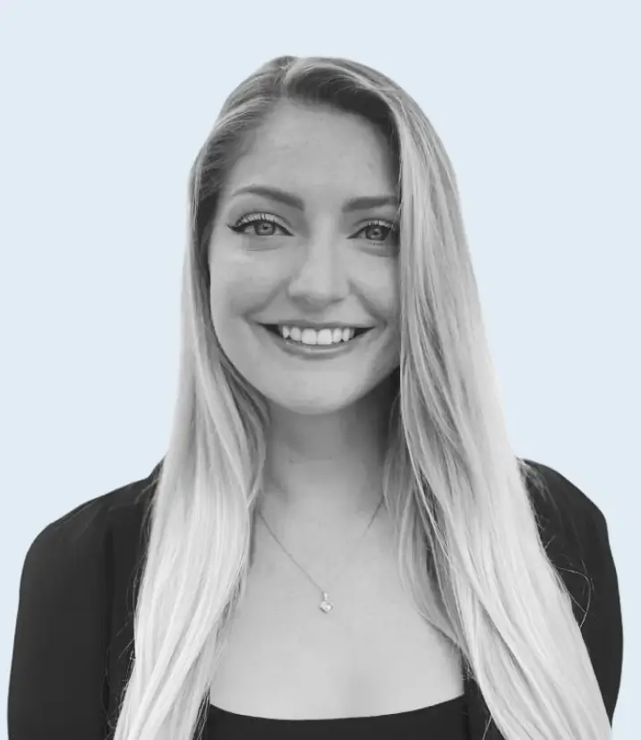 Smiling woman with long blonde hair wearing a black top and hoop earrings against a light background.