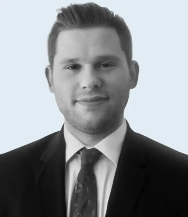 Portrait of a man in a suit and tie, with short styled hair, smiling slightly against a light background.