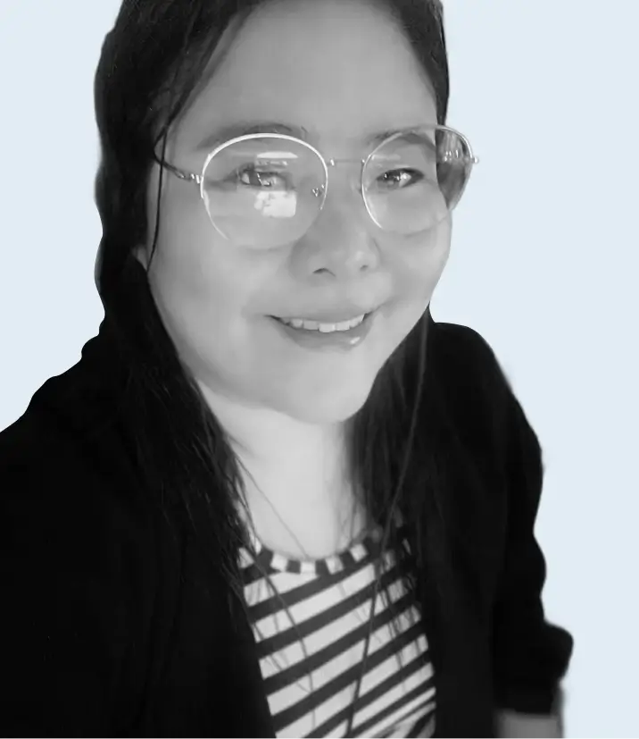 Smiling woman with long dark hair, wearing round glasses, a striped shirt, and a dark jacket.