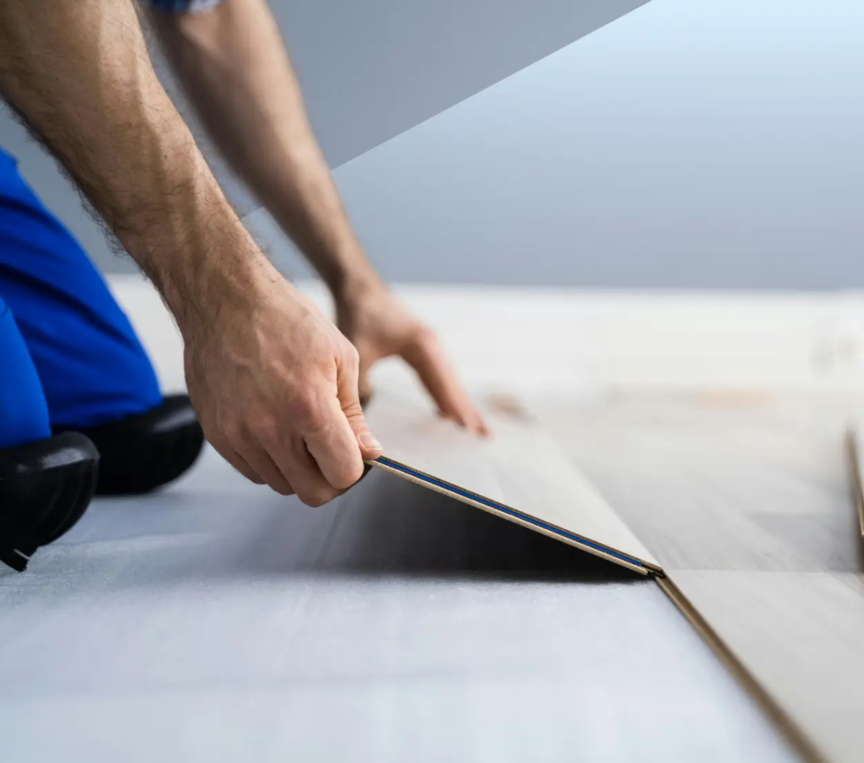 Person installing light-colored interlocking wood floor panels.