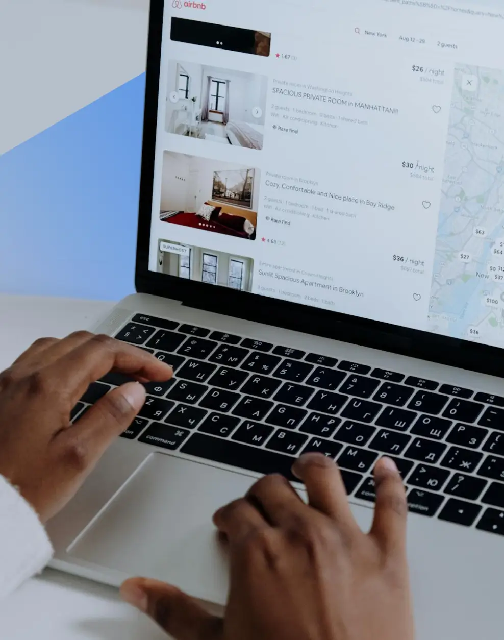 Person browsing Airbnb listings with photos and prices on a laptop keyboard with Cyrillic letters.