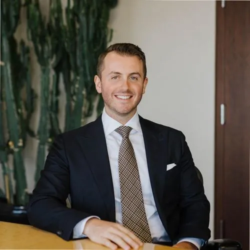A portrait taken of the Founder and Managing Partner of Reach, Avery Shopsowitz.  He is wearing a black suit with a biege and brown striped tie.