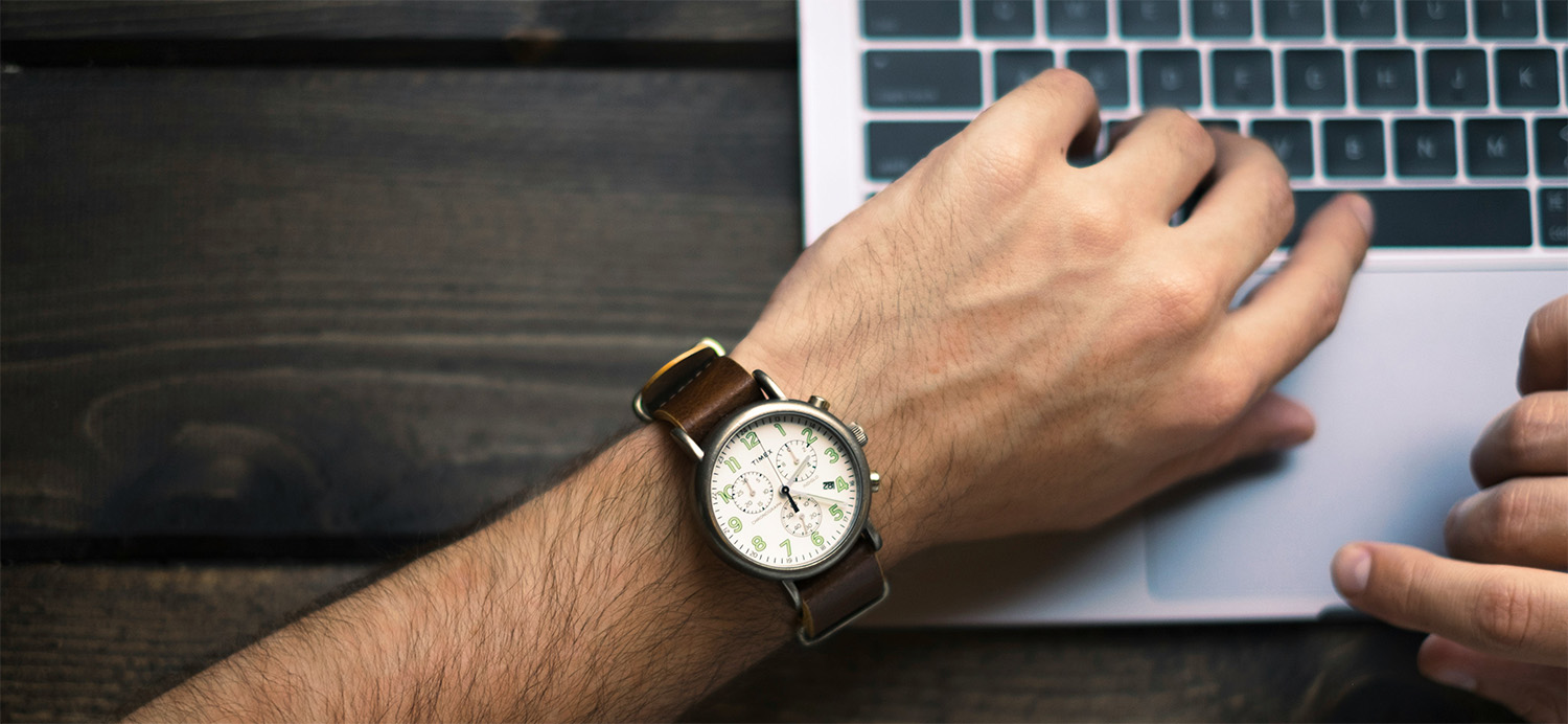 Close-up of a person wearing a wristwatch while working on a laptop, symbolizing time tracking and billable hours.