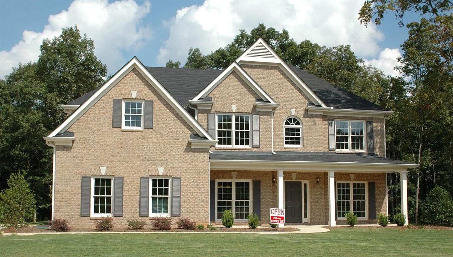 Two-story brick house with gray shutters and an open house sign on the front lawn.