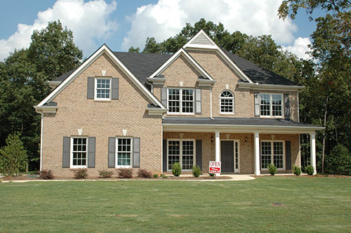 Two-story brick house with gray shutters and an open house sign on the front lawn.